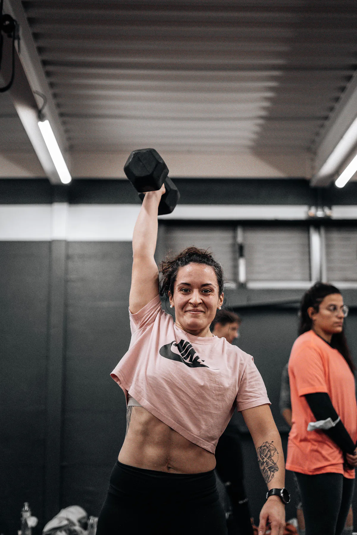 Eine Sportlerin hebt im Fitnessstudio eine Kurzhantel über den Kopf.